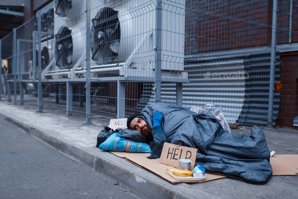 Dirty homeless with help sign lies on city street