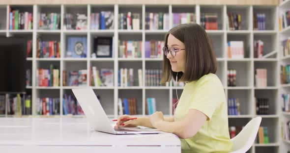 Young Woman is Smiling Sitting at a Desk with a Laptop Working in the Library