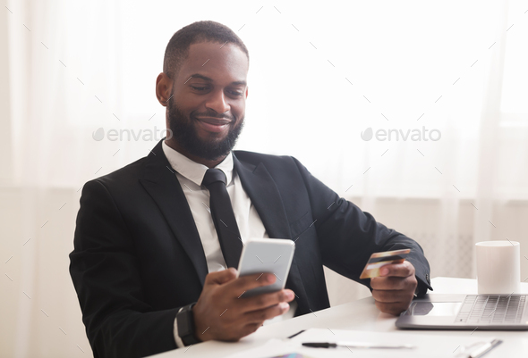 Afro businessman holding credit card, making purchases online by phone
