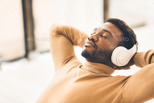 Smiling black businessman leaning back listening to music