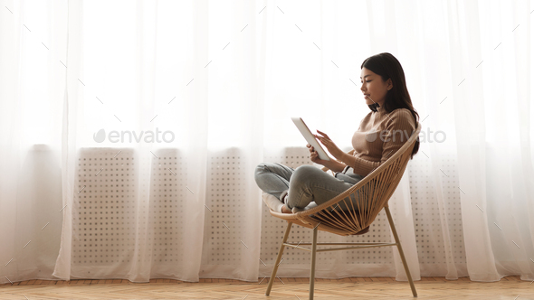 Lazy weekend. Girl using tablet, sitting in wicker chair