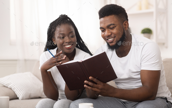 Afro couple looking at notepad at home, checking plans and to-do-list