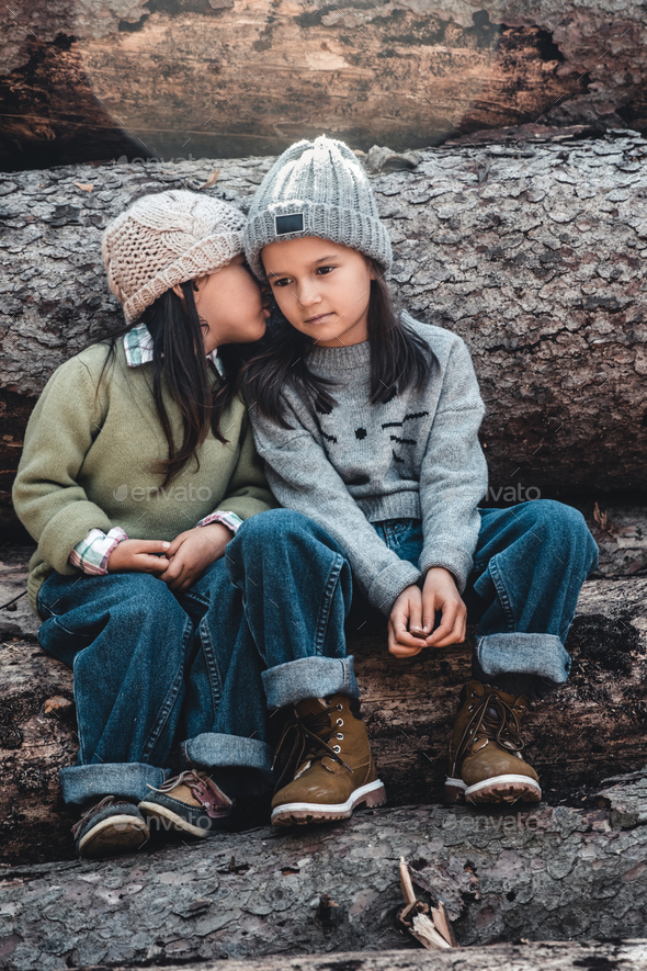 Little girl whispers a secret to her sistersitting on the logs