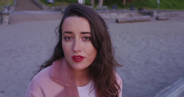A gorgeous, young woman sitting on a beach turns and smiles brightly at the camera alt