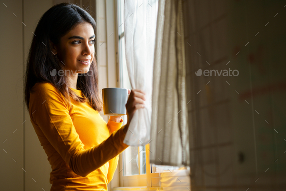 Persian woman drinking coffee while looking through the window