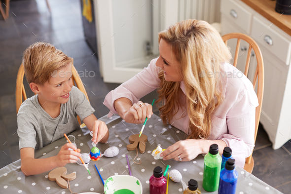 Mother With Son Sitting At Table Decorating Eggs For Easter At Home