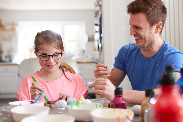 Father With Daughter Sitting At Table Decorating Eggs For Easter At Home