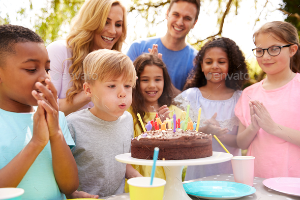 Boy Blows Out Candles As He Celebrates Birthday With Party For Parents And Friends In Garden At Home