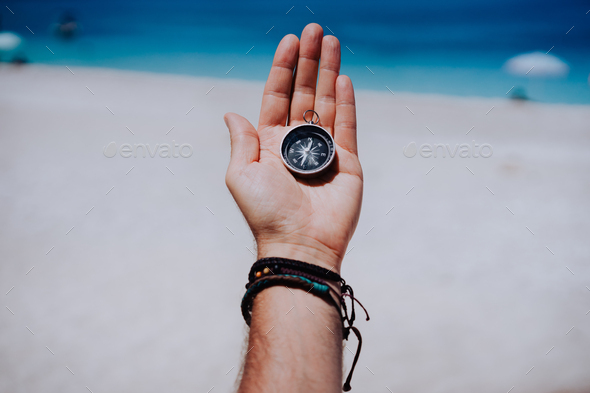 One open stretched hand palm with black metal compass on the sandy beach. Find your wish goal way