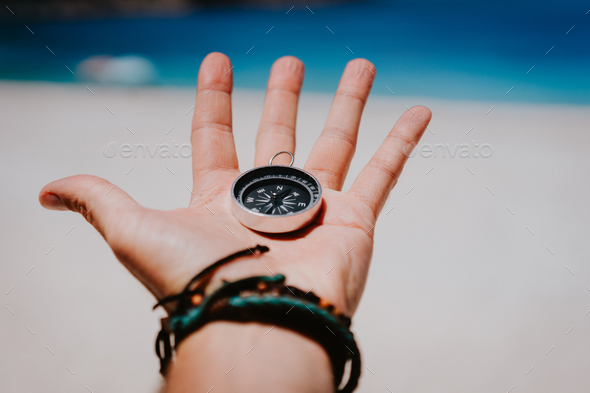 Open palm with stretched fingers holding black metal compass against white sandy beach. Find your - Stock Photo - Images