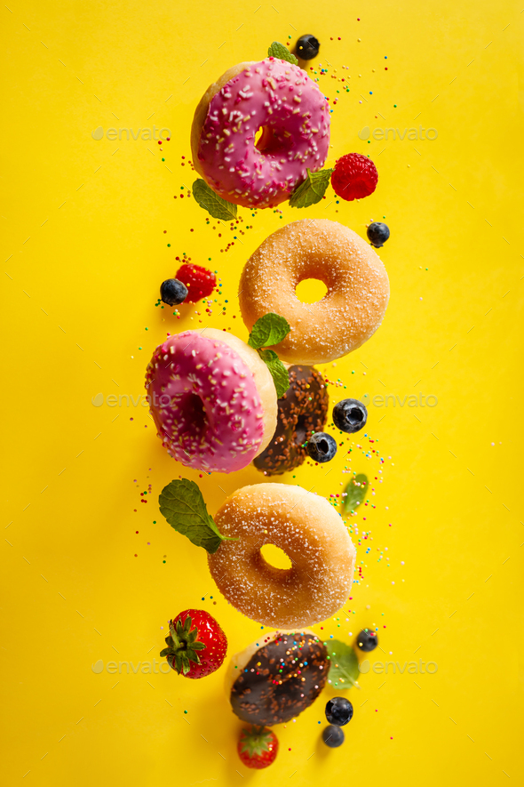Various decorated doughnuts with sprinkles and berries in motion falling on yelloy background - Stock Photo - Images