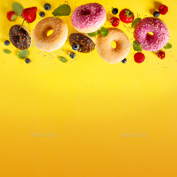 Various decorated doughnuts with sprinkles and berries in motion falling on yelloy background - Stock Photo - Images