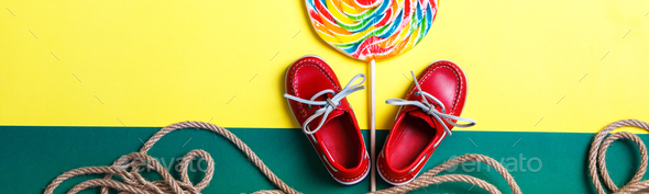 Banner of Small red boat shoes near big multi-colored lollipop and rope on colored background.
