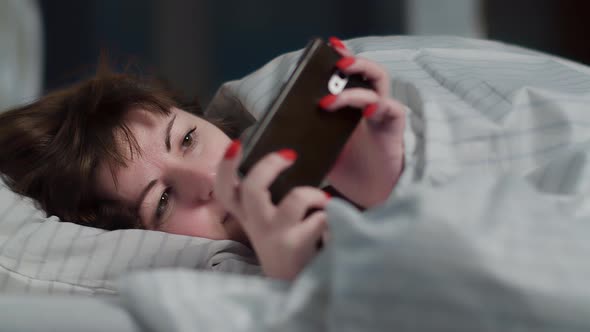 Sleepy Brunette Brunette Woman Lies on the Bed and Uses the Phone at Night Read Some Information