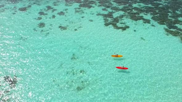 Aerial drone view of a man and woman couple kayaking around a tropical island. alt