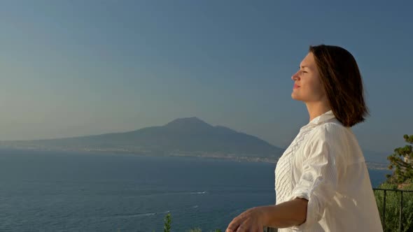 Young Woman Stands on a Balcony with a Beautiful View of the Sea and Mountains