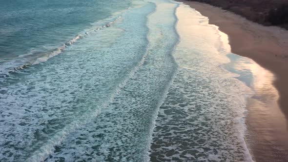 Aerial view of waves crash to shore at sunset