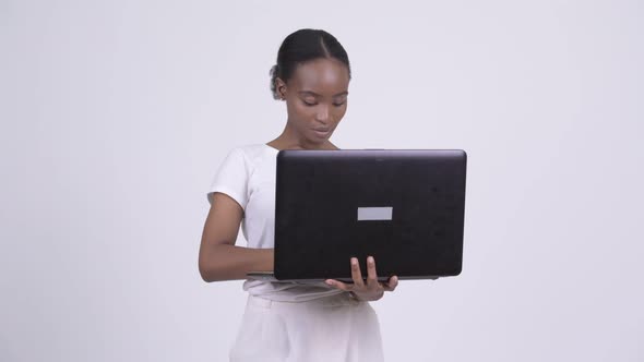 Happy Young Beautiful African Woman Thinking While Using Laptop alt