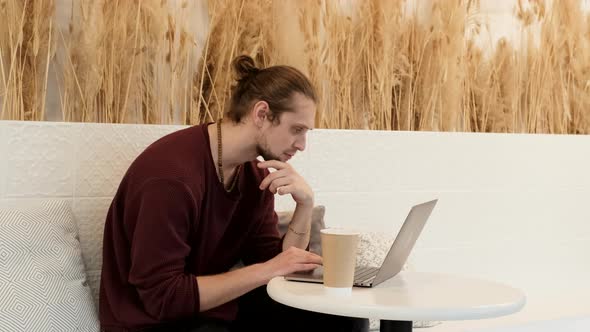 A Young European Man Is Thoughtful, Looks at The Monitor Screen, Is Working on A New Online alt