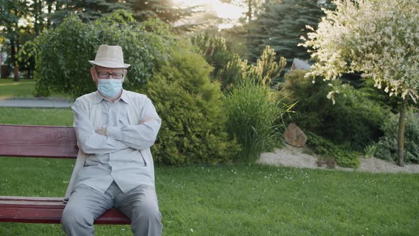 Cultured Senior Man in Medical Mask Looking Into Camera While Sitting on Bench alt