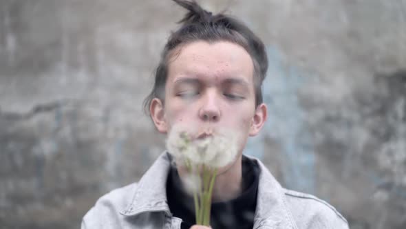 A Teen Boy is Blowing on a Dandelions