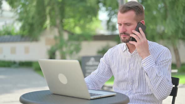 Middle Aged Man Talking on Smartphone in Outdoor Cafe alt
