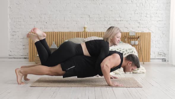 Man Doing Push Up Exercises at Home with His Woman Is Lying Above on His Back