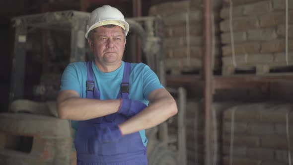Portrait of Serious Caucasian Man in Blue Uniform and White Helmet Posing at Factory or Plant alt