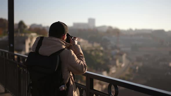 Traveling Photographer Man Takes Photos with Camera While Standing on Bridge