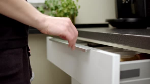 Girl or Woman in Black Tshirt and Short Shorts Walks Over to Cutlery Drawer and Pick Up Shiny Chrome alt