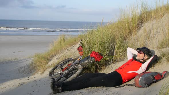 A man resting on the beach by his mountain bike. alt