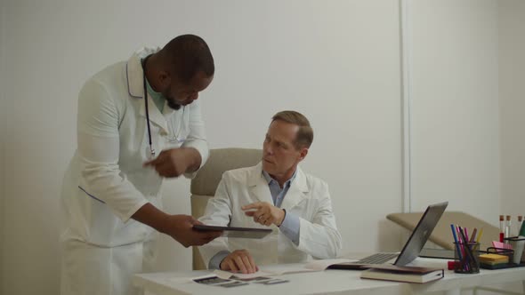 African American Doctor and Experienced Male Colleague Discussing Medical Test Report on Tablet Pc alt