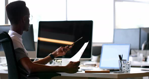 Male executive checking document at desk  alt