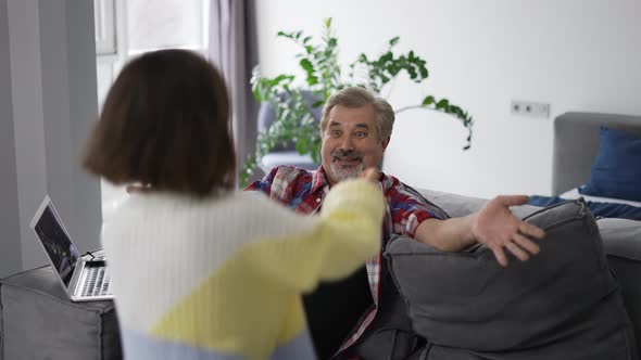 Elderly Man Sitting on Couch When His Granddaughter Running Up and Hugging Him alt