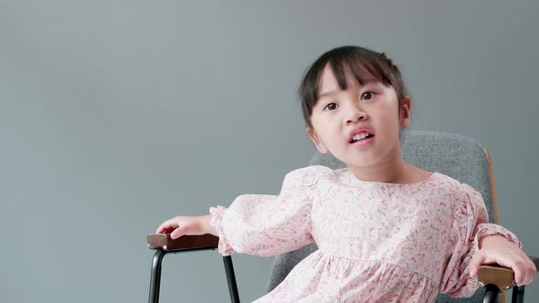 Cheerful and happy Asian children 3 Years old Sitting in a chair in front of the gray background. alt