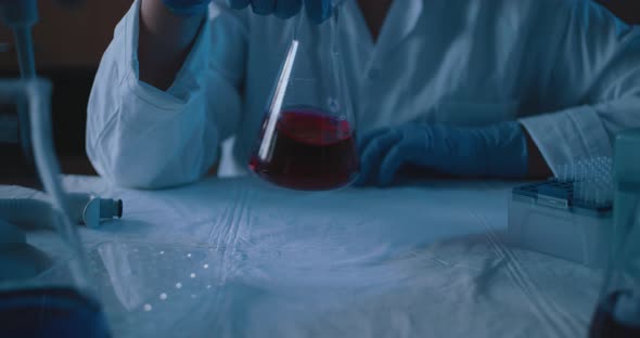 Female research scientist mixing up a conical flask with red liquid, slow motion alt