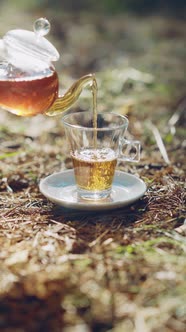 Woman pours tea from a glass teapot into a glass Cup