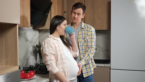 Pregnant Woman Drinks Tea and Husband Strokes Belly Softly alt