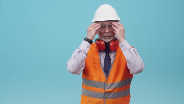Adult Man Engineer with a Helmet and Work Vest Puts on Protective Glasses and Folds Arms on Chest in alt