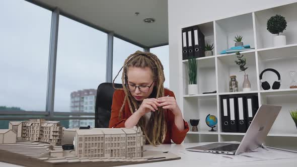 Female Architect with Dreadlocks Working with Wooden Model of New Buildings alt