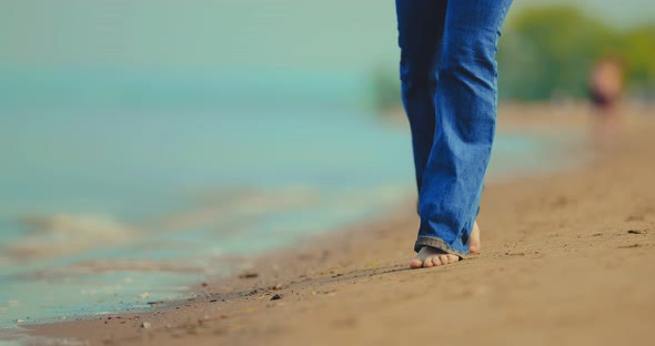 Woman in Wet Jeans and Bare Feet Walks in the Sand on the Beach alt