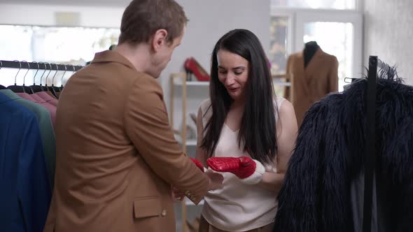 Joyful Happy Woman Trying on Red Mittens Smiling Looking at Camera As Blurred Cheerful Gay Man alt