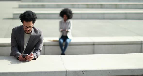 Businessman using smartphone at train station with woman in background alt