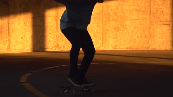 Silhouette of a young man skateboarding in a parking garage at sunset. alt