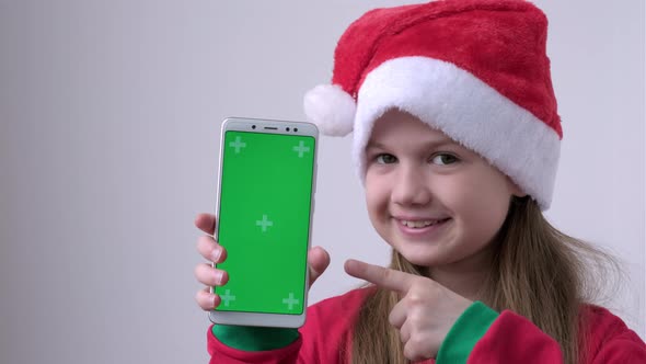 Little Girl in Christmas Santa Hat Shows Phone with Green Screen alt