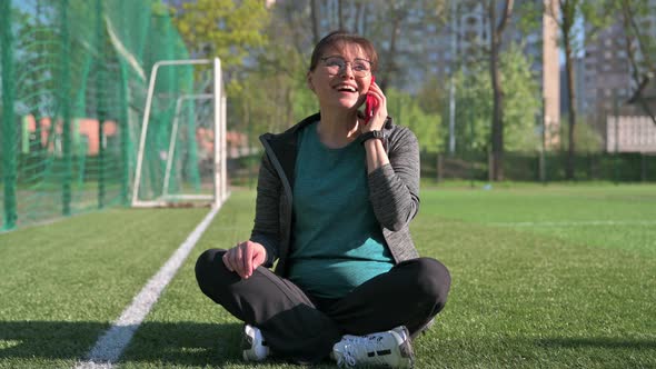 Middle Aged Woman in Sportswear Talking on the Phone While Sitting at Sports Outdoor Stadium