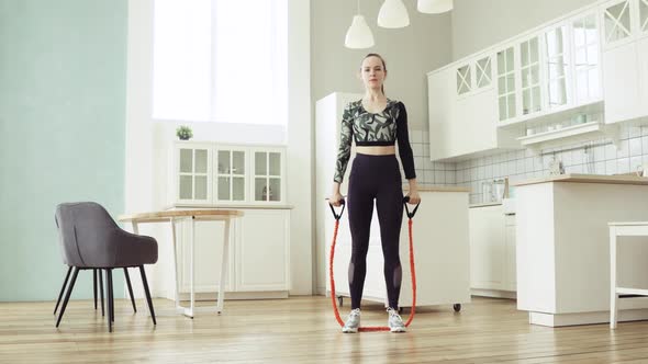 Woman Using Sport Expander for Squatting at Fitness Training in Kitchen at Home.