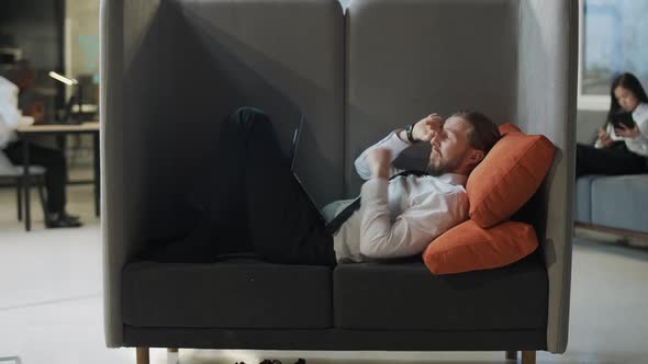 Office Manager Lies in a Large Chair and Works at a Laptop Office Work in an Open Space a Tired Man alt