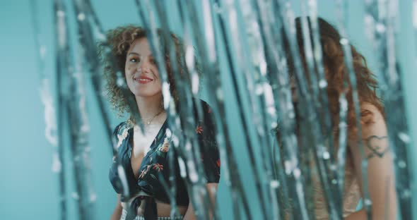 Two women dance together behind shimmering curtain alt