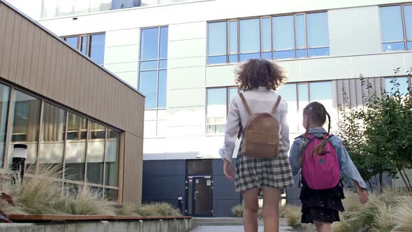 Two Schoolgirls of Different Ages with Backpacks Go to School Holding Hands